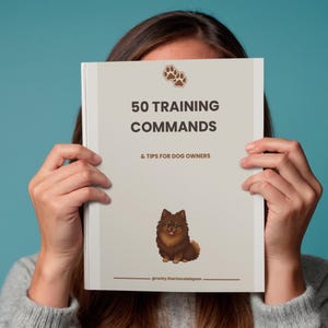 以下が含まれることがあります： 50 TRAINING COMMANDS & TIPS FOR DOG OWNERSというタイトルのライトベージュの小冊子。表紙の上部には茶色の肉球アイコン、中央にはふわふわした茶色のポメラニアンのイラスト、下部には@rocky.thechocolatepomというテキストが記載されています。
