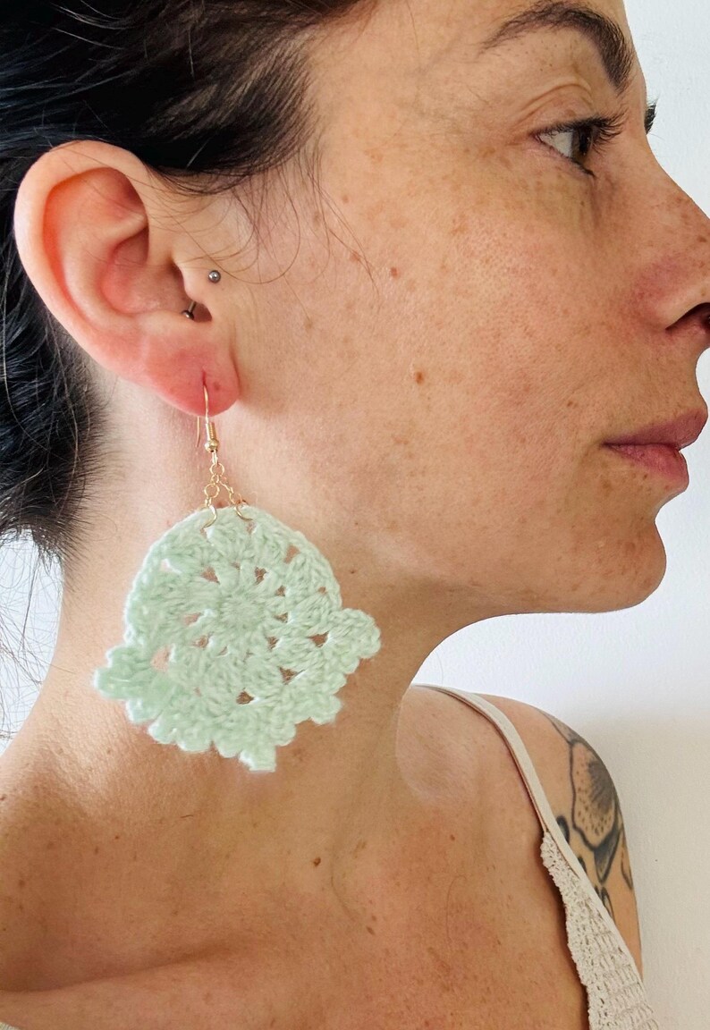 May include: A pale mint green crochet earring featuring a circular, openwork floral pattern. The lightweight, circular textile piece is attached to a thin gold-toned metal hook, designed for insertion into a pierced earlobe for decorative wear.