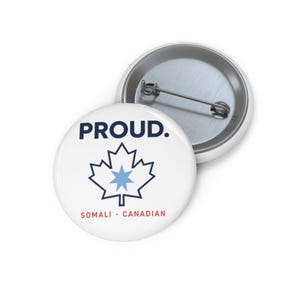 May include: A round white pin-back button featuring the text PROUD. in dark blue, a dark blue maple leaf outline with a light blue star in the center, and the text SOMALI • CANADIAN in red at the bottom. The back shows a metal pin mechanism.
