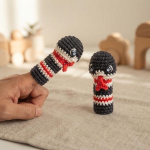 Puede incluir: Dos marionetas de dedo tejidas a ganchillo con forma de serpiente, con rayas horizontales negras, blancas y rojas. Cada marioneta tiene una cabeza redondeada con dos pequeños ojos de plástico negro y una lengua roja bífida.