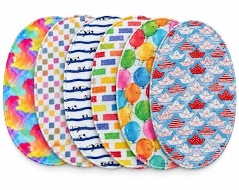 Puede incluir: Un conjunto de seis almohadillas de tela ovaladas con varios patrones coloridos, incluyendo tie-dye, un tablero de ajedrez multicolor, rayas azules con caras de panda, un diseño de ladrillos arcoíris, globos flotantes y barcos de papel.