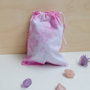 Könnte beinhalten: Eine rosa-weiße Batik-Kordeltasche mit einer Blume und Kristallen auf einer weißen Oberfläche.