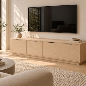 May include: A long, rectangular light-toned wooden media console featuring four cabinet doors with thin, horizontal black metal handles. The unit sits on a low base and is positioned against a wall beneath a large, flat-screen television.