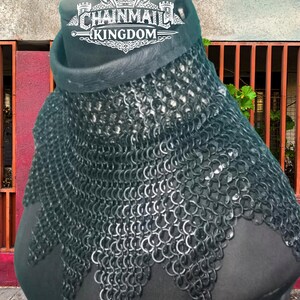 May include: A black chainmail gorget featuring a leather collar and a scalloped edge design. The metal rings are linked together to form a protective neck and shoulder covering. The logo for Chainmail Kingdom is visible at the top of the piece.