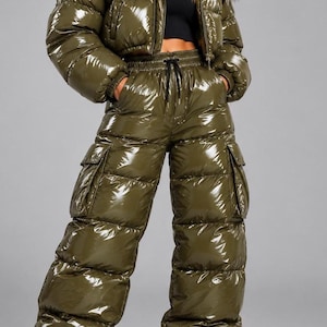 Pode incluir: Um casaco acolchoado verde-oliva brilhante com capuz de pelo sintético e calças cargo acolchoadas de cintura subida a combinar. O casaco tem um fecho de correr frontal e as calças incluem uma cintura com cordão e bolsos laterais grandes.