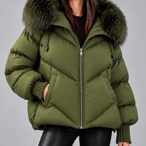 May include: An olive green puffer jacket featuring a large hood with a thick faux fur trim, a central silver zipper closure, and ribbed knit cuffs. The jacket has a quilted chevron pattern, two side pockets, and a high collar design.