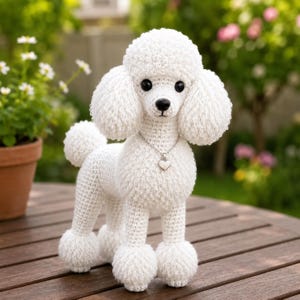May include: A white crocheted poodle figurine featuring a textured, curly yarn body, black bead eyes, a black stitched nose, and a silver-toned chain necklace with a small heart-shaped pendant resting against its chest.
