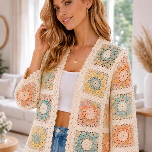May include: A long-sleeved open-front cardigan made of cream-colored crochet granny squares. Each square features a central floral pattern in pastel shades of peach, yellow, and light blue. The garment has a scalloped edge along the front opening.