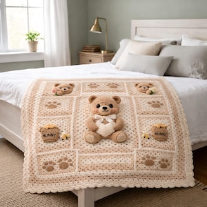 Può includere: Una coperta all'uncinetto beige con un orsacchiotto tridimensionale al centro che tiene un cuore bianco, circondato da quadrati con facce d'orso, impronte di zampe e vasi di miele con l'etichetta "HUNNY" e api, con un bordo smerlato.