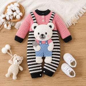 May include: A long-sleeved crochet romper featuring a pink top with two white buttons, black and white horizontal stripes on the legs, and a large cream-colored bear appliqué wearing blue overalls. Includes a matching small crochet bear toy.