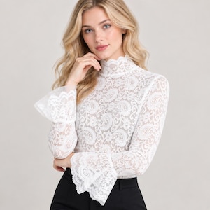 May include: A white long-sleeve top made of intricate floral and paisley lace fabric. The garment features a high mock neck collar and dramatic flared bell sleeves with scalloped edges. The lace pattern is consistent throughout the bodice and sleeves.
