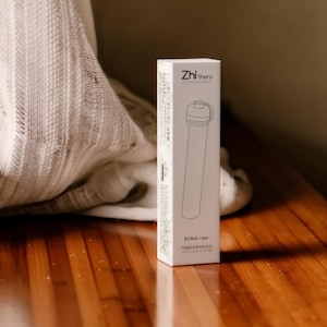 Könnte beinhalten: Eine weiße, rechteckige Produktverpackung mit der Aufschrift Zhi thera und einer schwarzen Strichzeichnung eines zylindrischen Behälters. Die Verpackung zeigt den Text 6.5mL/pcs sowie weitere gedruckte Informationen auf der Seitenfläche.