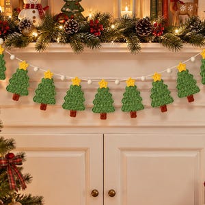 May include: A festive garland featuring nine crocheted green Christmas trees with brown trunks and yellow star toppers, strung together on a white cord interspersed with small white felt balls, hanging horizontally against a white fireplace mantel.
