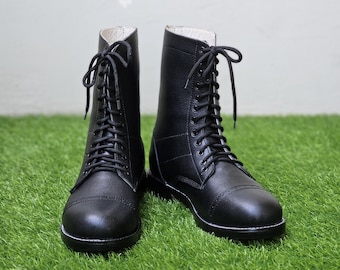 May include: A pair of black leather lace-up boots featuring a rounded toe, a high-top shaft, and black laces threaded through metal eyelets. The boots have a smooth finish, a reinforced toe cap, and a solid black sole, providing a structured appearance.