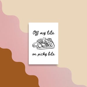 May include: A white rectangular greeting card featuring a black line drawing of a charcuterie board filled with various food items. The text "Off my tits" is printed above the illustration, and "on picky bits" is printed below the drawing.