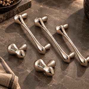 May include: A set of five polished silver-toned metal cabinet hardware pieces, including three elongated bar pulls and two smaller knob pulls, all featuring a smooth, rounded, bone-like shape with a reflective, high-gloss finish.