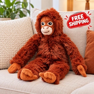 May include: A plush orangutan stuffed animal with long, shaggy, rust-colored fur, a light tan face, and dark eyes. The toy features long arms and legs with textured, lighter orange hands and feet, sitting upright with a friendly expression.