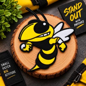 May include: An embroidered patch featuring a cartoon wasp with a yellow and black striped body, white wings, and a determined expression. The patch is centered on a circular wooden slice, surrounded by black fabric labels with the text STAND OUT WITH PATCHES and SMALL PATCH BIG ATTITUDE.