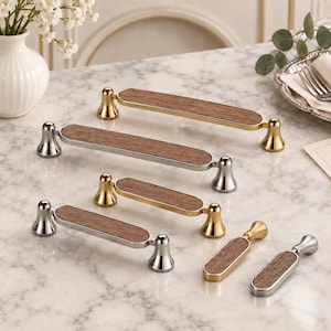 May include: A collection of cabinet hardware featuring elongated drawer pulls and knobs with a central wood inlay. The hardware comes in polished gold and silver finishes, each with two flared, bell-shaped mounting posts at the ends.
