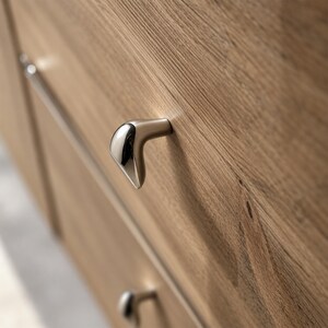 May include: A light brown wooden drawer front featuring a distinctively shaped, metallic cabinet knob with a polished chrome finish on the front face and a satin nickel finish on the sides, mounted on a horizontal grain wood surface.
