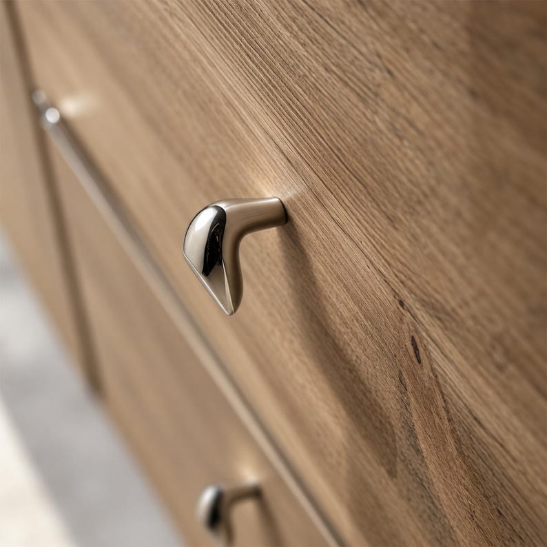 May include: A light brown wooden drawer front featuring a distinctively shaped, metallic cabinet knob with a polished chrome finish on the front face and a satin nickel finish on the sides, mounted on a horizontal grain wood surface.
