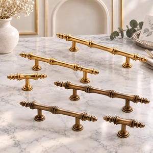 May include: A collection of six brass cabinet pulls and knobs featuring a segmented bamboo-inspired design. The hardware pieces vary in length and finish, ranging from bright polished gold tones to a darker, muted antique brass patina.