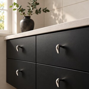 May include: Four matte black cabinet drawers featuring small, polished silver-toned metal pulls with a curved, teardrop-inspired shape. The drawers are arranged in a two-by-two grid, providing a clean, uniform look for storage cabinetry.