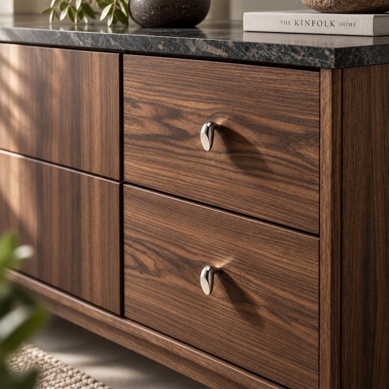 May include: A dark wood cabinet featuring two stacked drawers with prominent grain patterns. Each drawer is equipped with a single, small, polished silver-toned metal knob. The cabinet is topped with a dark, speckled stone surface.