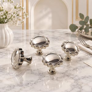 May include: Four polished silver-toned metal cabinet knobs with a circular, reflective center and a scalloped, petal-like outer edge. Each knob features a smooth, rounded top and a sturdy base, designed for attachment to furniture or cabinetry.