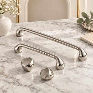 May include: A collection of polished silver-toned hardware including two long, curved cabinet pulls and two rounded, asymmetrical cabinet knobs. Each piece features a smooth, reflective metallic finish with rounded edges and a solid, heavy appearance.