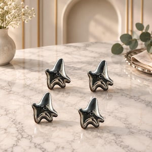 May include: Four small, metallic, silver-toned star-shaped figurines with smooth, reflective surfaces. Each star features a simple, engraved facial expression with two eyes and a small mouth, arranged in a group on a light-colored surface.