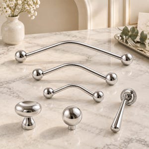 May include: A collection of polished chrome hardware including three arched cabinet pulls of varying lengths, one round mushroom-shaped knob, one spherical ball knob, and one vertical drop pull, all featuring a smooth, reflective metallic finish.