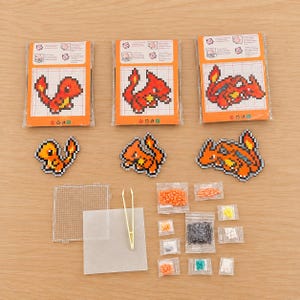 May include: A craft kit featuring three pixel art character designs, including printed instruction cards, finished bead figures, a clear square pegboard, a sheet of parchment paper, yellow plastic tweezers, and assorted small bags of colored plastic beads.