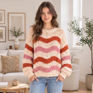 May include: A long-sleeve crochet sweater featuring a wavy striped pattern in cream, burnt orange, and dusty pink. The garment has a round neckline, ribbed cuffs, and a ribbed hem, constructed with an open-knit texture throughout the body.