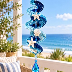 May include: A spiral-shaped hanging decoration featuring crocheted yarn in shades of navy, royal, and light blue. The piece is accented with two white starfish, one white seashell, clear glass beads, and a large, faceted blue crystal pendant.