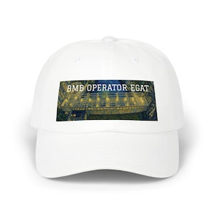 May include: A white baseball cap featuring a rectangular graphic print on the front. The print displays a dark, textured illustration of a dam structure with illuminated lights and the text BMB OPERATOR EGAT EST 1999 in white lettering.