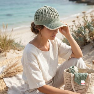May include: A sage green crochet baseball cap featuring a structured grid pattern on the crown and a solid brim with a white edge trim. The cap is crafted from yarn and displays a consistent stitch texture throughout the dome and visor area.
