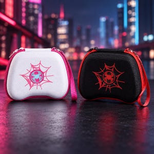 Könnte beinhalten: Zwei harte Controller-Transporttaschen, eine weiße mit pinkfarbenem Spinnennetz-Motiv und eine schwarze mit rotem Spinnennetz-Motiv. Jede Tasche verfügt über ein zentrales Spinnenemblem, einen Reißverschluss und eine passende Handschlaufe.