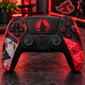 Op de afbeelding: Een zwarte draadloze videogamecontroller met een rood en zwart grafisch ontwerp. De linkerkant toont een karakterillustratie, terwijl de rechterkant rode wolkenmotieven bevat. Het centrale touchpad is voorzien van een cirkelvormig rood embleem.