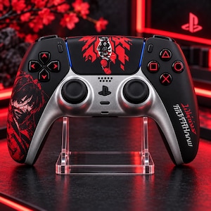 May include: A black and silver wireless video game controller featuring red graphic illustrations of an anime character and abstract patterns. The controller includes red directional buttons, a central PlayStation logo, and text in a stylized font.