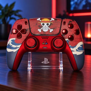 Puede incluir: Un mando de videojuegos inalámbrico rojo y azul oscuro con el emblema de la calavera y las tibias cruzadas de One Piece en el panel táctil central. El cuerpo muestra un patrón de mapa y una ola estilizada, con botones y joysticks rojo metálico.