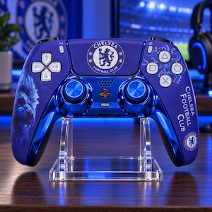 Puede incluir: Un mando de juego inalámbrico azul con el logotipo del Chelsea Football Club, un gráfico de un león en la empuñadura izquierda y el texto Chelsea Football Club en la derecha. El mando tiene botones de acción blancos, joysticks azul metálico y un logotipo de PlayStation.