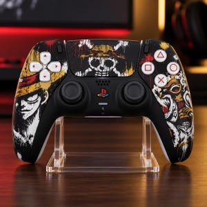 Könnte beinhalten: Ein schwarzer kabelloser Videospiel-Controller mit einem individuellen Grafikdruck eines Charakters mit Strohhut und Totenkopf-Emblem. Der Controller verfügt über weiße Richtungstasten, ein zentrales PlayStation-Logo und Standard-Aktionstasten.