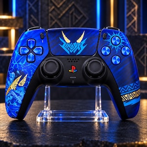 Puede incluir: Un mando de videojuego inalámbrico azul con un diseño gráfico personalizado que incluye patrones de rayos, iconos de cuernos dorados y motivos tribales geométricos. El mando incluye un logotipo central de PlayStation, joysticks negros y botones azules.