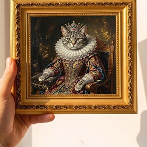 Könnte beinhalten: Ein gerahmtes Porträt einer getigerten Katze in prunkvoller königlicher Kleidung, inklusive weißem Spitzenkragen und einer juwelenbesetzten Krone. Die Katze sitzt auf einem Thron vor dunklem Hintergrund. Der Rahmen ist goldfarben mit Relief.