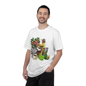 Puede incluir: Una camiseta blanca con un estampado gráfico colorido de una persona con sombrero cosechando granos de café de una planta, acompañada de una cafetera italiana plateada, una taza de café, un mortero de madera y un aguacate.