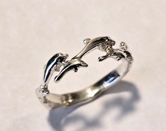 May include: A silver ring featuring a design of three dolphins jumping in a circle.