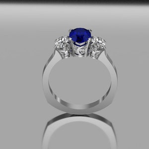 May include: A silver ring featuring a central, round, deep blue gemstone, with two smaller, clear gemstones either side. The ring has a modern, geometric design with a polished finish. The gemstones are set in a prong setting.