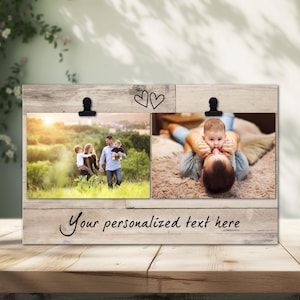 Może przedstawiać: Drewniana ramka na zdjęcia z dwoma miejscami na zdjęcia. Każde miejsce ma czarny klips do trzymania zdjęcia. Ramka ma napis "Your personalized text here" i dwa rysunki serc. Ramka stoi na drewnianym stole.