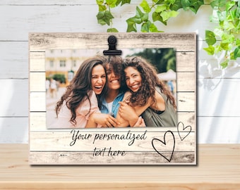 Op de afbeelding: Een wit houten fotolijst met een clip om een foto vast te houden. De lijst heeft een verweerde houten look en de tekst "Your personalized text here" staat onderaan. Er zijn twee handgetekende harten aan de rechterkant van de lijst.